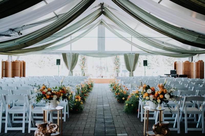 Stunning draped tent ceremony space with green silk ceiling and vibrant floral aisle by InStyle Events