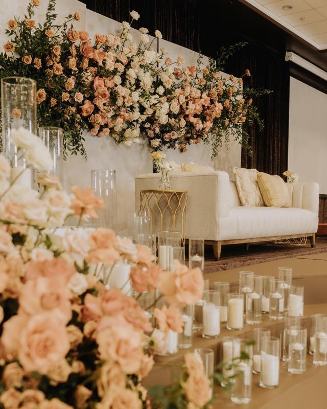 Elegant reception stage with cascading peach floral wall and white sofa by InStyle Events