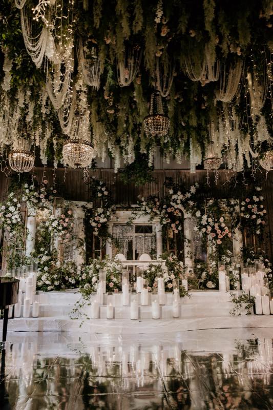 Grand wedding reception with crystal chandeliers, greenery ceiling, and reflective dance floor by InStyle Events