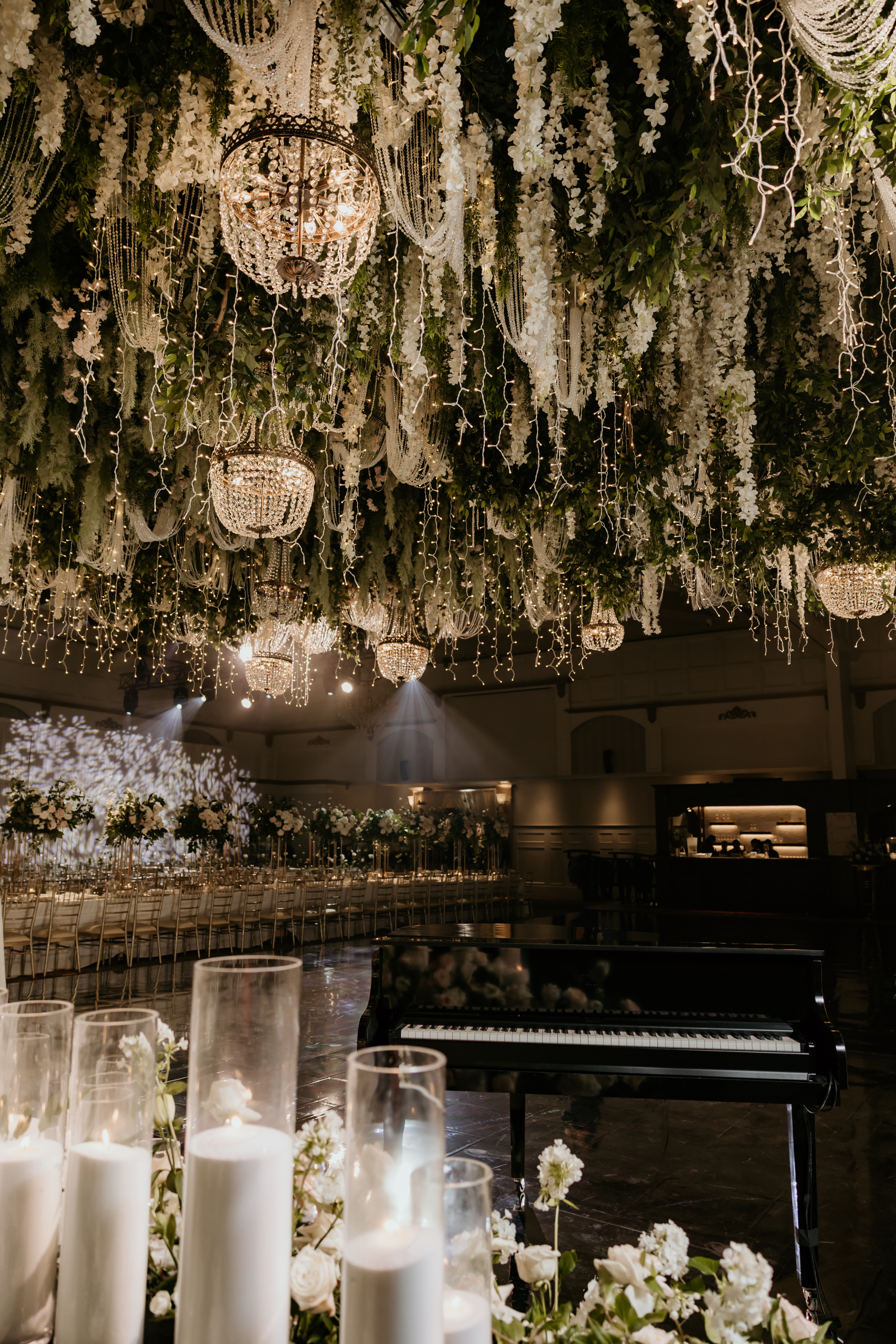 Crystal ball chandeliers illuminating a grand wedding venue with hanging wisteria and pillar candles by InStyle Events